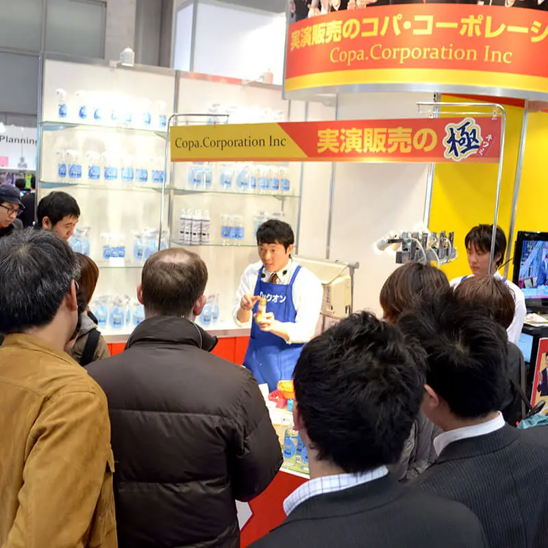 展示会のブースで実演販売士を囲む人垣
